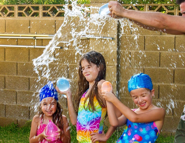 The Arms of a Father Break a Water Balloon Over the Heads of His Three Daughters